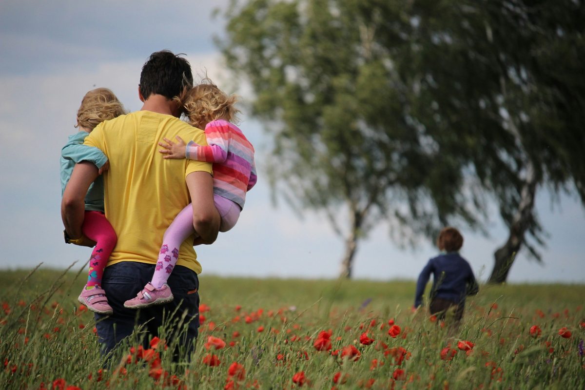 A father carrying his two children through a wildflower field
